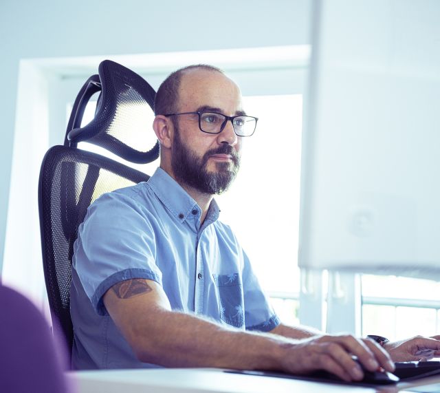 Ein Mann sitz vor dem Computer auf seinem Bürostuhl