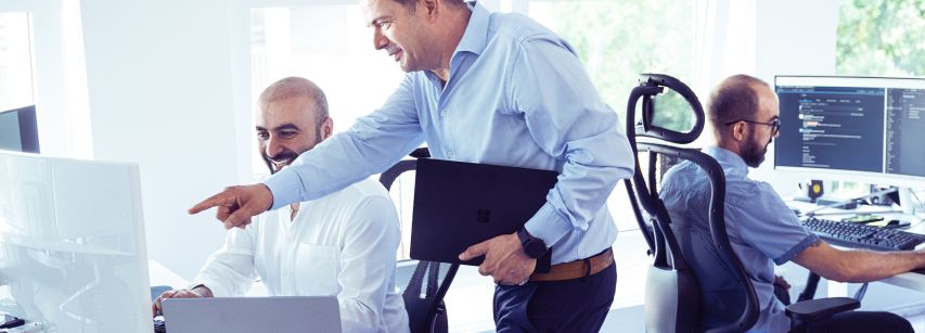 Herr Heymanns unterhält sich mit Mitarbeiter vor einem Bildschirm